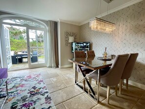 A dining area with a glass table, cushioned chairs, and a chandelier. - Beachhouse Seaside 3 - Beachhouse Seaside 3 Rantum, 107qm mit 3 Schlafzimmern für bis zu 6 Personen (Sylt)