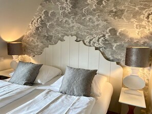 A bed with white linens and grey pillows, flanked by two bedside tables with lamps, against a wall with a cloud-patterned design. - Beachhouse Seaside 3 - Beachhouse Seaside 3 Rantum, 107qm mit 3 Schlafzimmern für bis zu 6 Personen (Sylt)