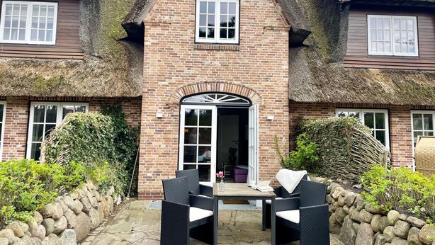 A traditional brick house with a thatched roof, a central entrance, and a patio with outdoor furniture. - Beachhouse Seaside 3 - Beachhouse Seaside 3 Rantum, 107qm mit 3 Schlafzimmern für bis zu 6 Personen (Sylt)