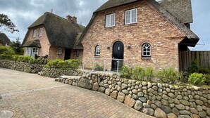 A traditional brick house with a thatched roof, a stone wall, and a paved driveway. - Beachhouse Seaside 3 - Beachhouse Seaside 3 Rantum, 107qm mit 3 Schlafzimmern für bis zu 6 Personen (Sylt)