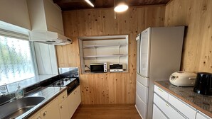 Een kleine keuken met houten wanden, een gasfornuis, een magnetron, een broodrooster en een koelkast.