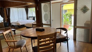 Een kamer met houten vloeren, een bed, een slaapbank, een eettafel met stoelen en een schuifdeur van glas die uitkomt op een terras.