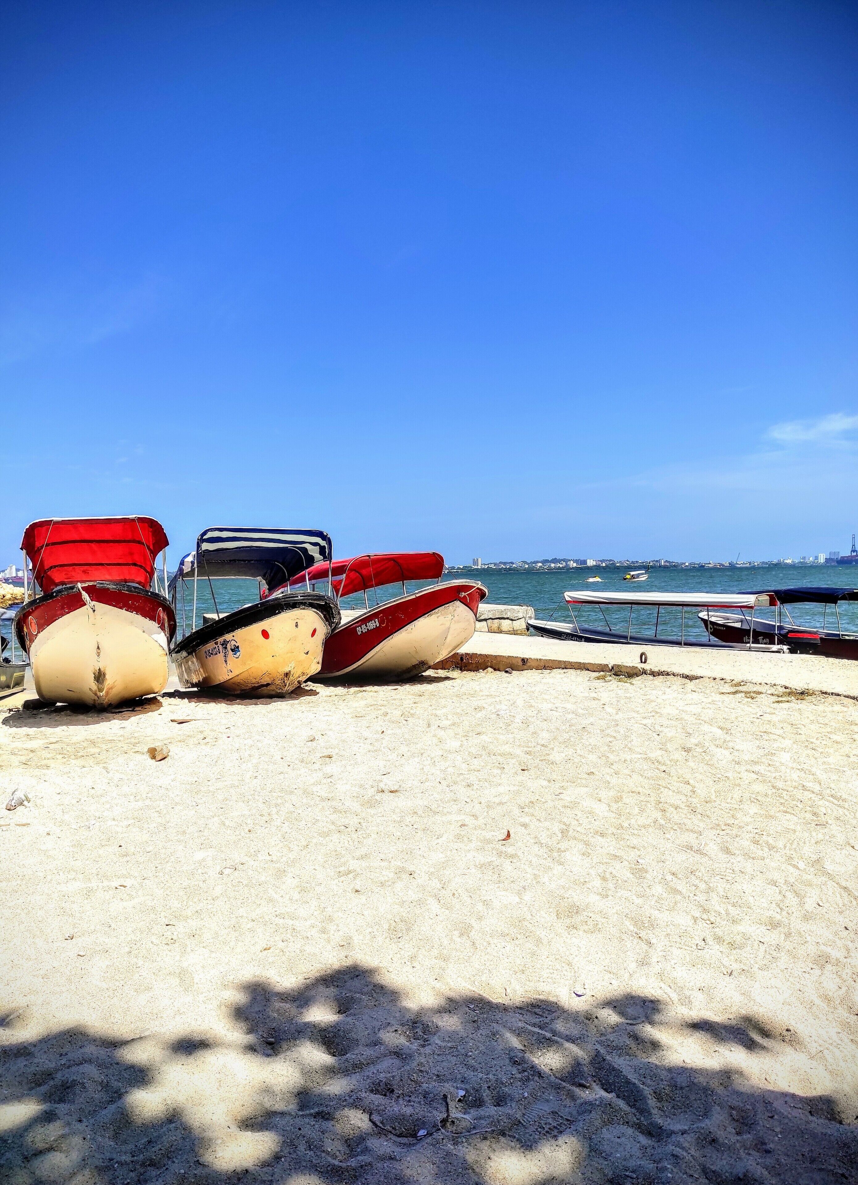 A sandy beach with several boats, including red and white canoes, and a clear blue sky.
