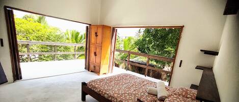 A bedroom with a bed, a ceiling fan, and a view of greenery outside.