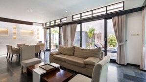 Een moderne hotellobby met een bank, stoelen, een salontafel en grote ramen voorzien van gordijnen.