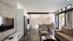 Een moderne woonkamer met een flatscreen televisie, een bank, een salontafel en een eethoek met stoelen.