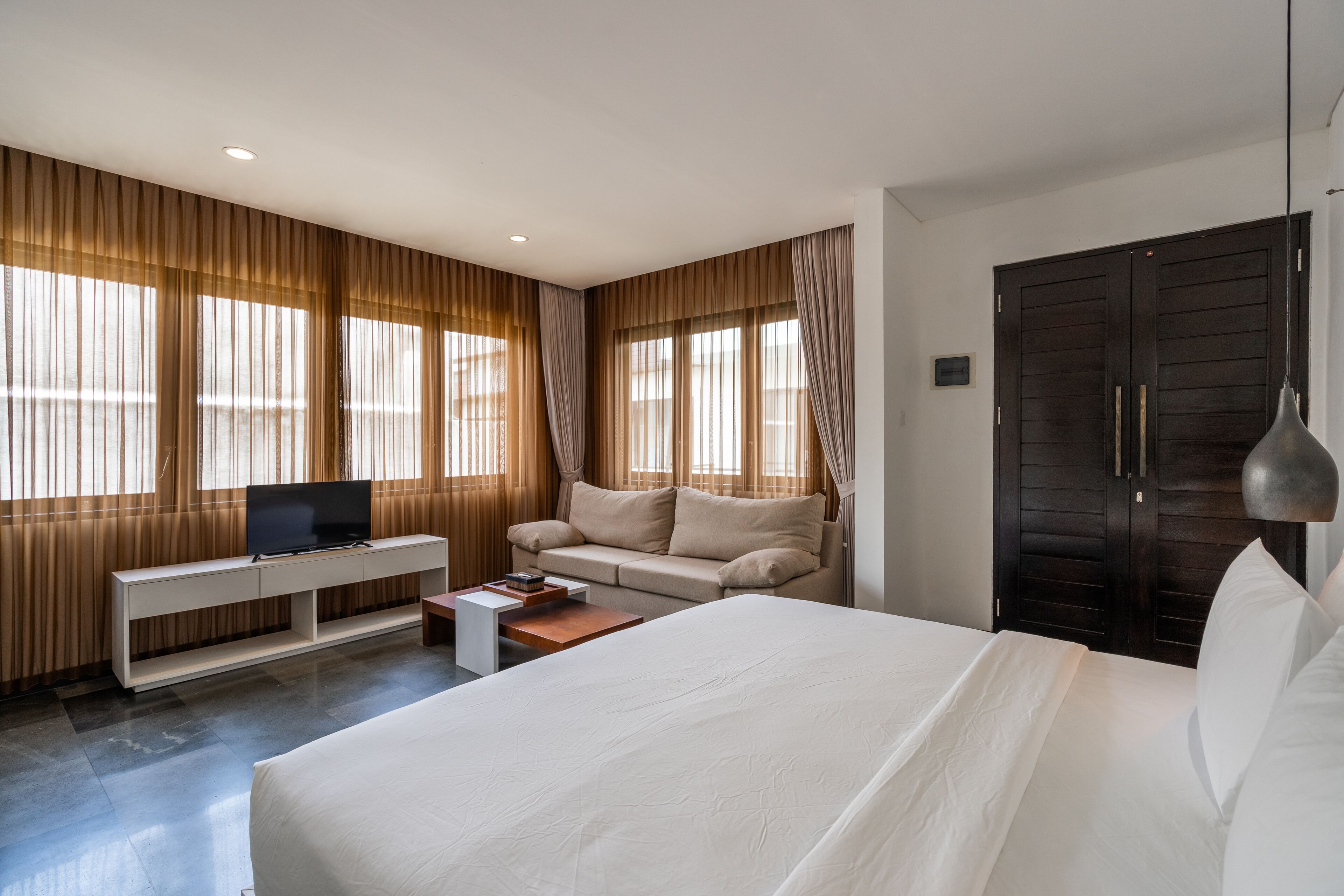 A modern hotel room with a large bed, a sofa, a TV on a console table, and a wardrobe.