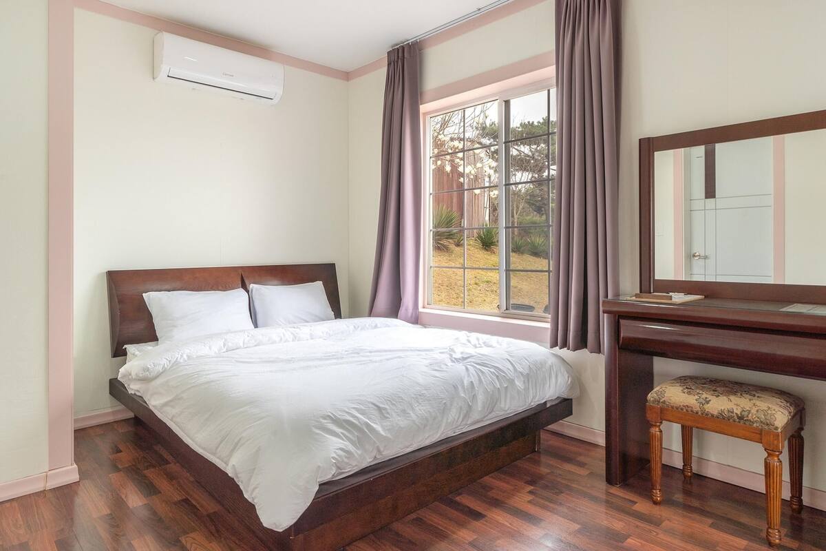 Une chambre à coucher avec un lit en bois, une table de chevet, un miroir et une fenêtre avec des rideaux.