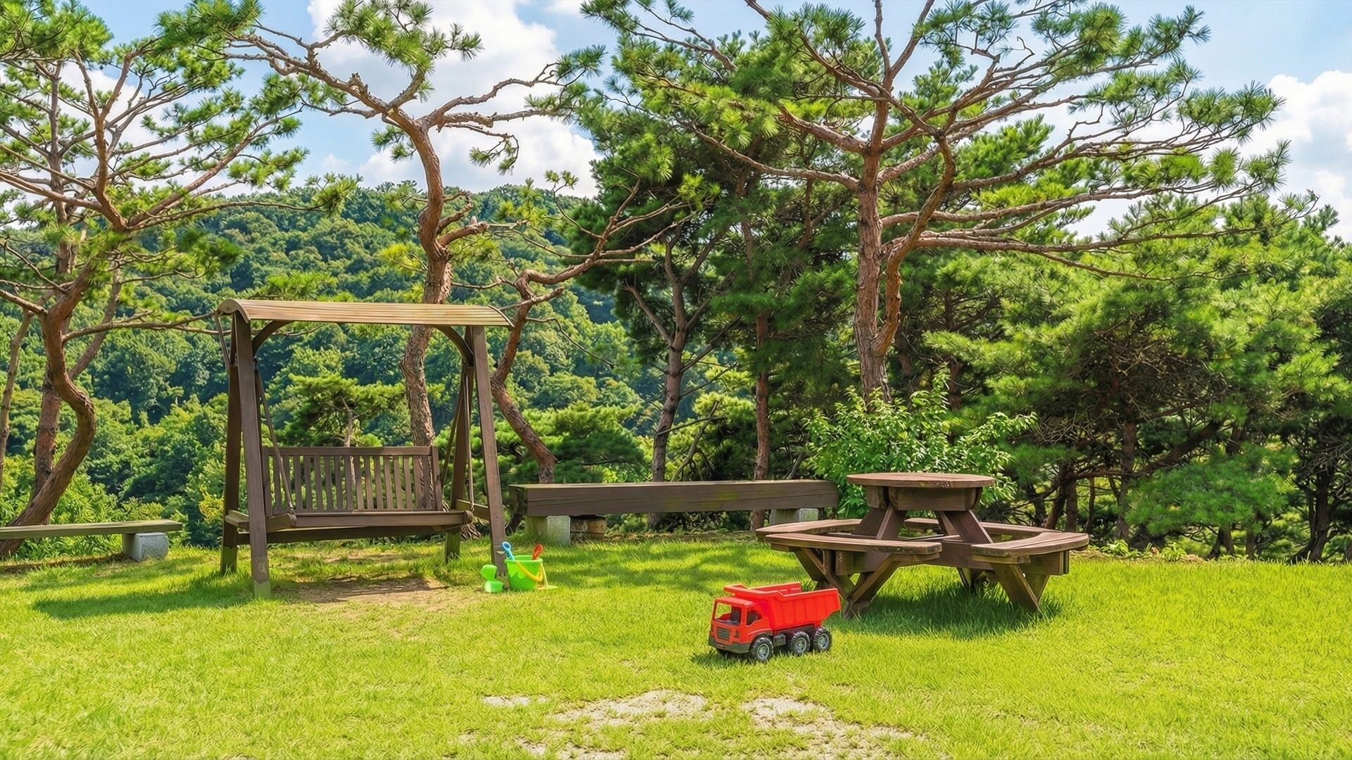 A wooden swing set, picnic table, and a small red toy truck in a grassy outdoor area with trees.