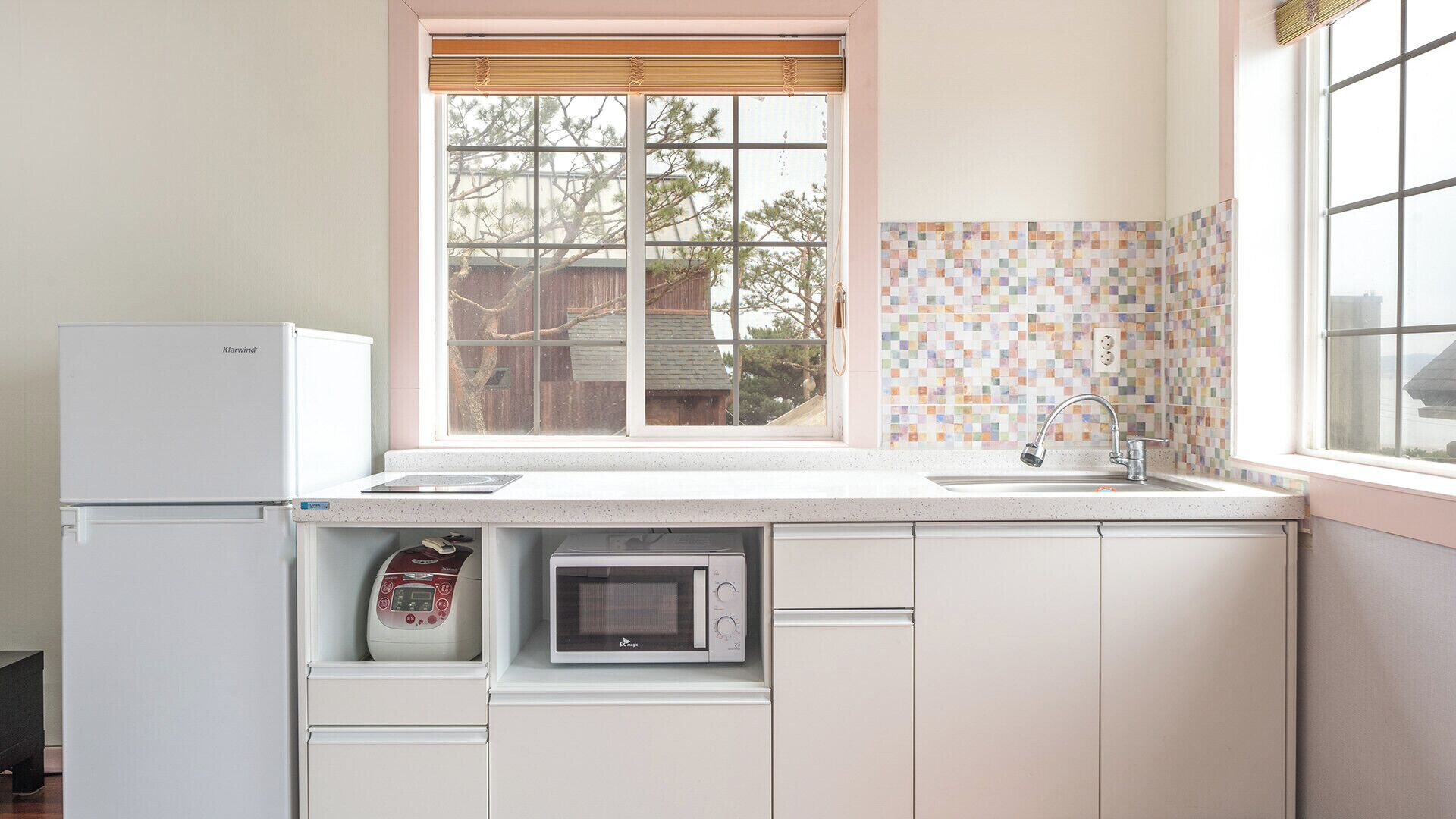 Una cocina con refrigerador, microondas y ventana con vista a árboles.