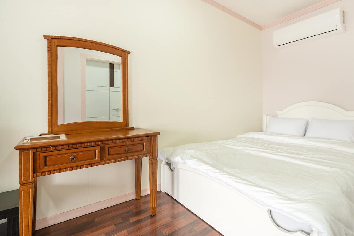 Une chambre avec une commode en bois, un lit avec une literie blanche et un appareil de climatisation fixé au mur.