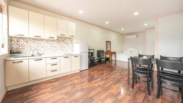 A compact hotel room with a kitchenette, a bed, a small dining area, and a bathroom.