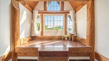 A room with a sloped ceiling, wooden beams, a large window with curtains, and a wooden floor.