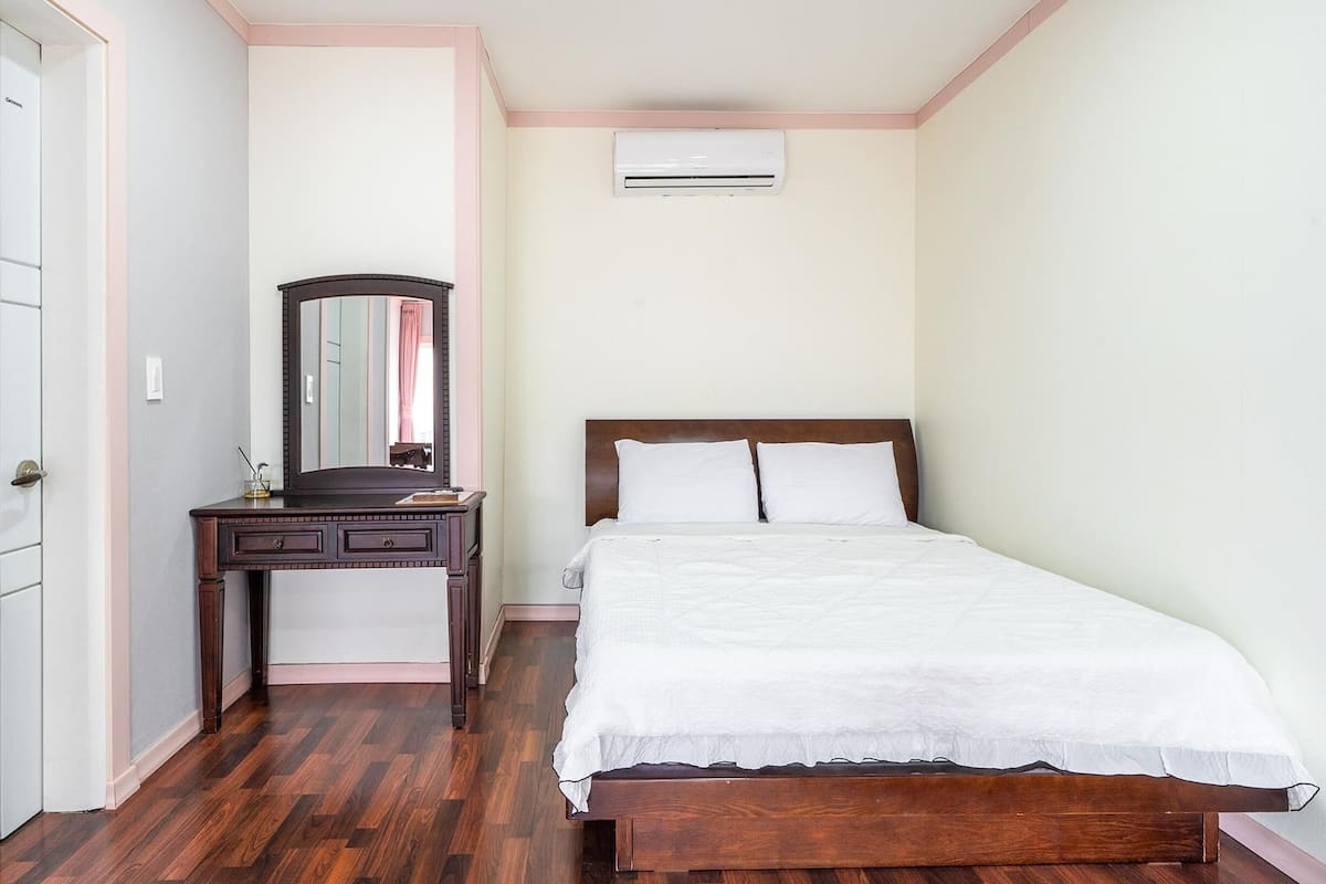 Une chambre à coucher avec un lit en bois, une commode, un miroir et un appareil de climatisation.