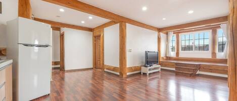 A spacious room with wooden beams, a white refrigerator, a television on a stand, and a window with a view.