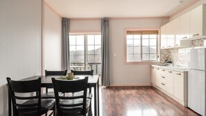 Une cuisine compacte avec un coin repas, comprenant une table avec des chaises, une fenêtre avec des rideaux et un réfrigérateur.