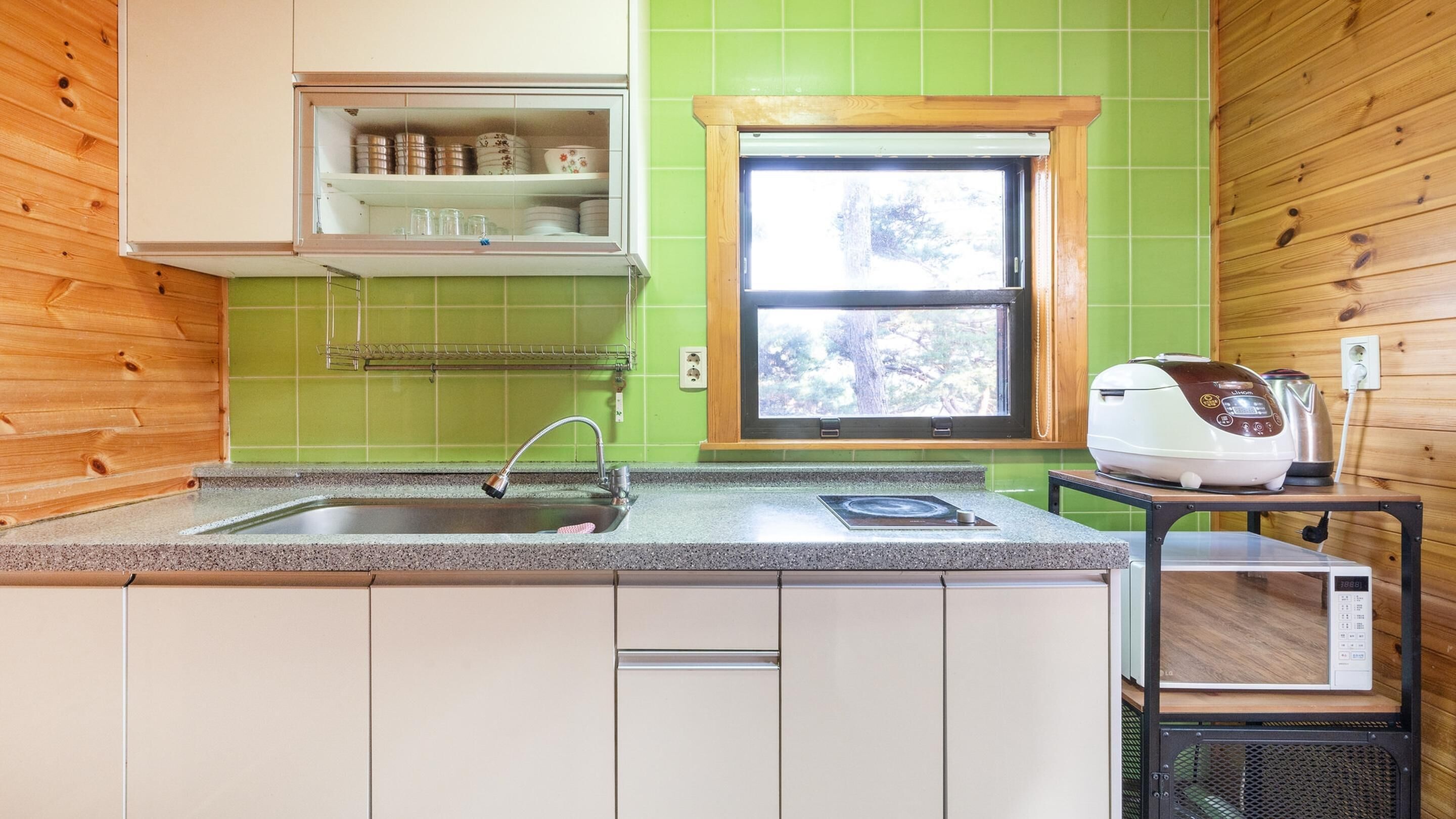 A kitchen with a granite countertop, a stainless steel sink, a window with a view of trees, and a microwave on a wooden table.