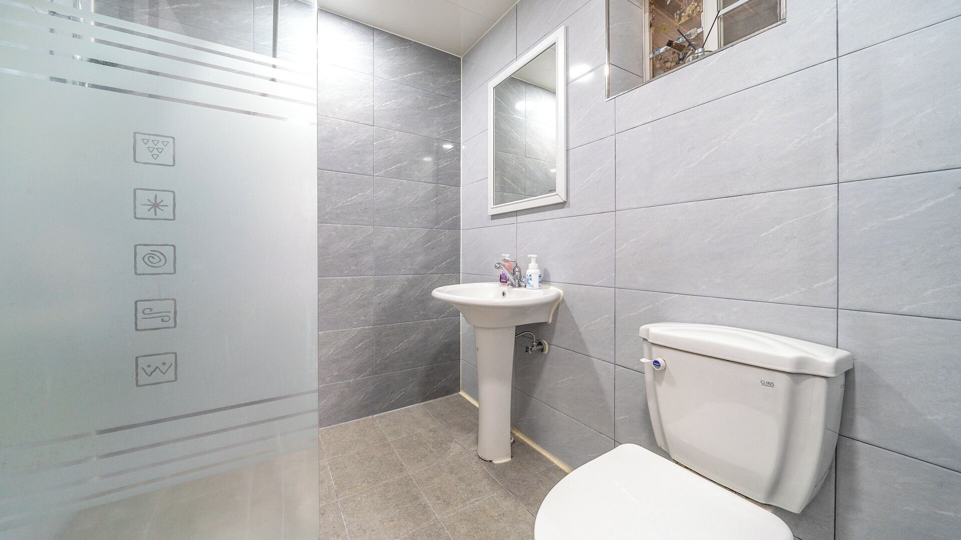 Ein Badezimmer mit einer weißen Toilette, einem Standwaschbecken und einem Spiegel darüber.