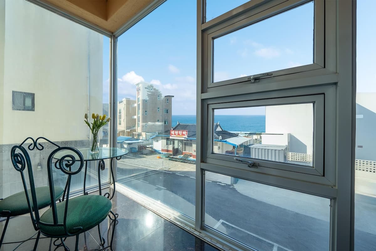 Un balcón con una mesa y sillas de vidrio, un jarrón con flores y vistas a edificios y al mar.