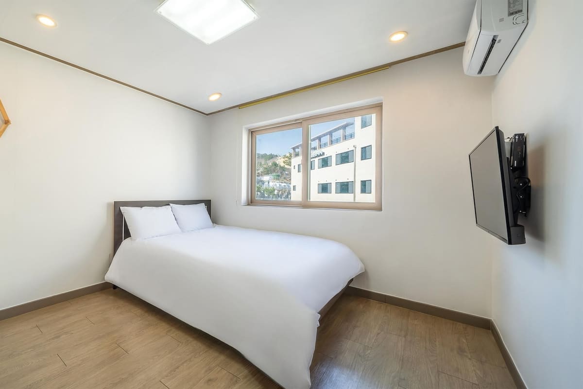 Un dormitorio con cama, ventana, televisor en la pared y luz en el techo.