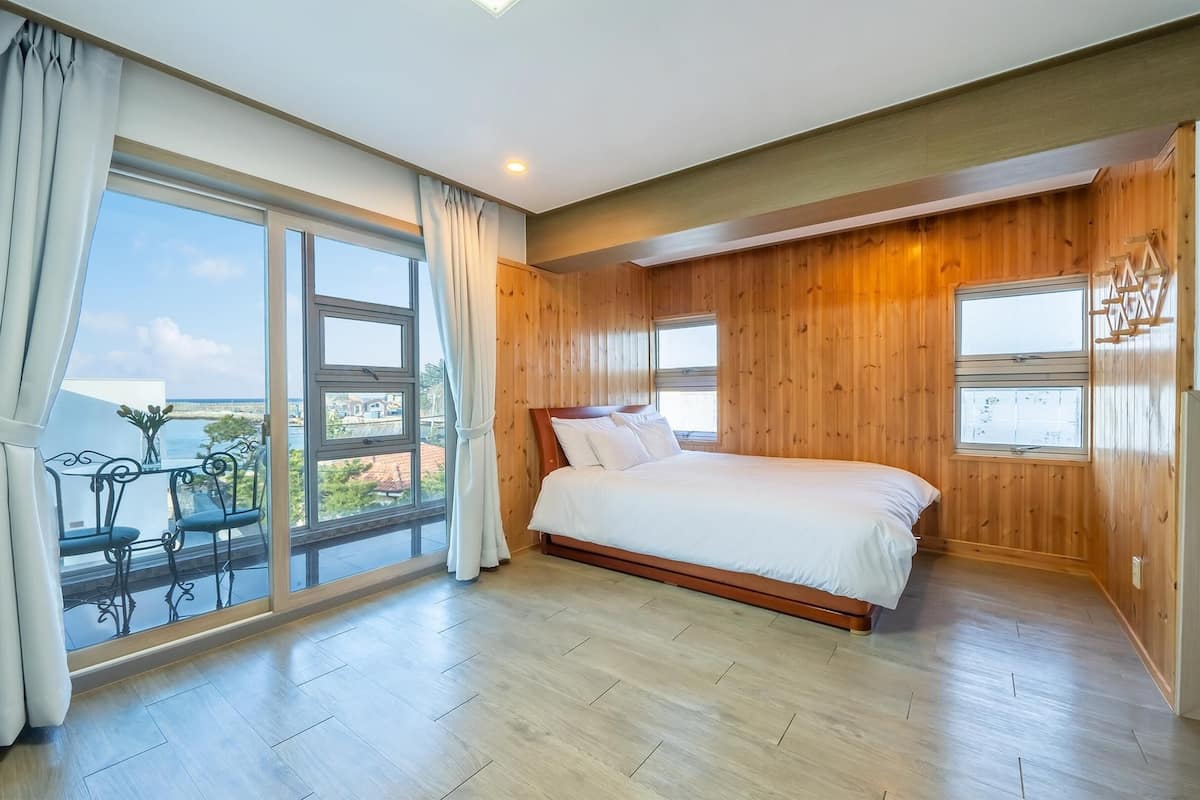 Un dormitorio con un ventanal grande, una cama y paneles de madera.
