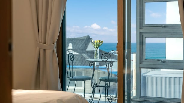 Una habitación con cama, ventana con vista al mar, mesa con sillas y un jarrón de flores.