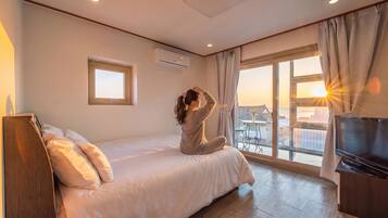 Habitación de hotel con cama, televisor, ventana con cortinas y vista al mar.
