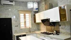 A modern kitchen with white cabinetry, a gas stove, and a built-in oven. There is a window with blinds, a sink, and a dishwasher. - Impeccable 4-Bed House in Lagos  Nigeria (Lagos)
