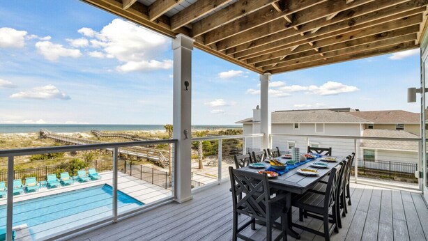 Un espacio al aire libre techado con piscina, mesa de comedor y sillas, con vista a una playa y al océano.