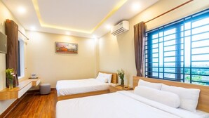 A hotel room with two beds, a wooden floor, a window with curtains, an air conditioner, and a painting on the wall. - Tai Nhien Homestay (Da Nang)