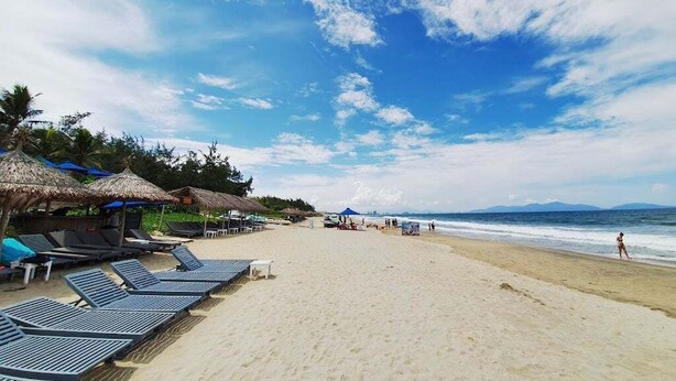 A beach with sun loungers and thatched umbrellas, a sandy shore, and the ocean in the background. - Tai Nhien Homestay (Da Nang)