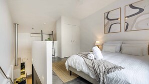 A modern bedroom with a bed, a bedside table with a lamp, a wardrobe, and abstract wall art.