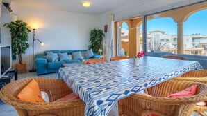 A modern living room with a blue sofa, wicker furniture, and a large table with a patterned tablecloth. - Magrana Over The Sea (Private Pool). by Interhome (Porto Cristo)