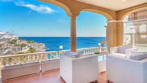 A balcony with white wicker furniture, a clear view of the sea, and a stone balustrade. - Magrana Over The Sea (Private Pool). by Interhome (Porto Cristo)