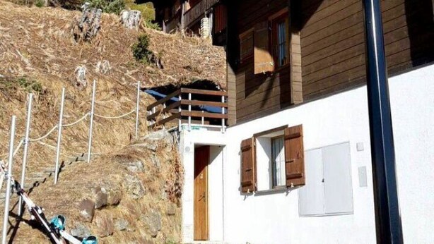 Una cabaña de madera con balcón, un soporte para esquíes y vistas despejadas de las colinas circundantes.