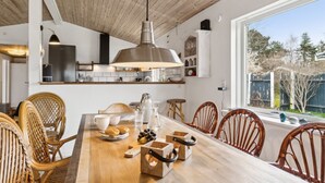Een moderne keuken met witte kasten, een houten plafond en een groot raam met uitzicht op een tuin.