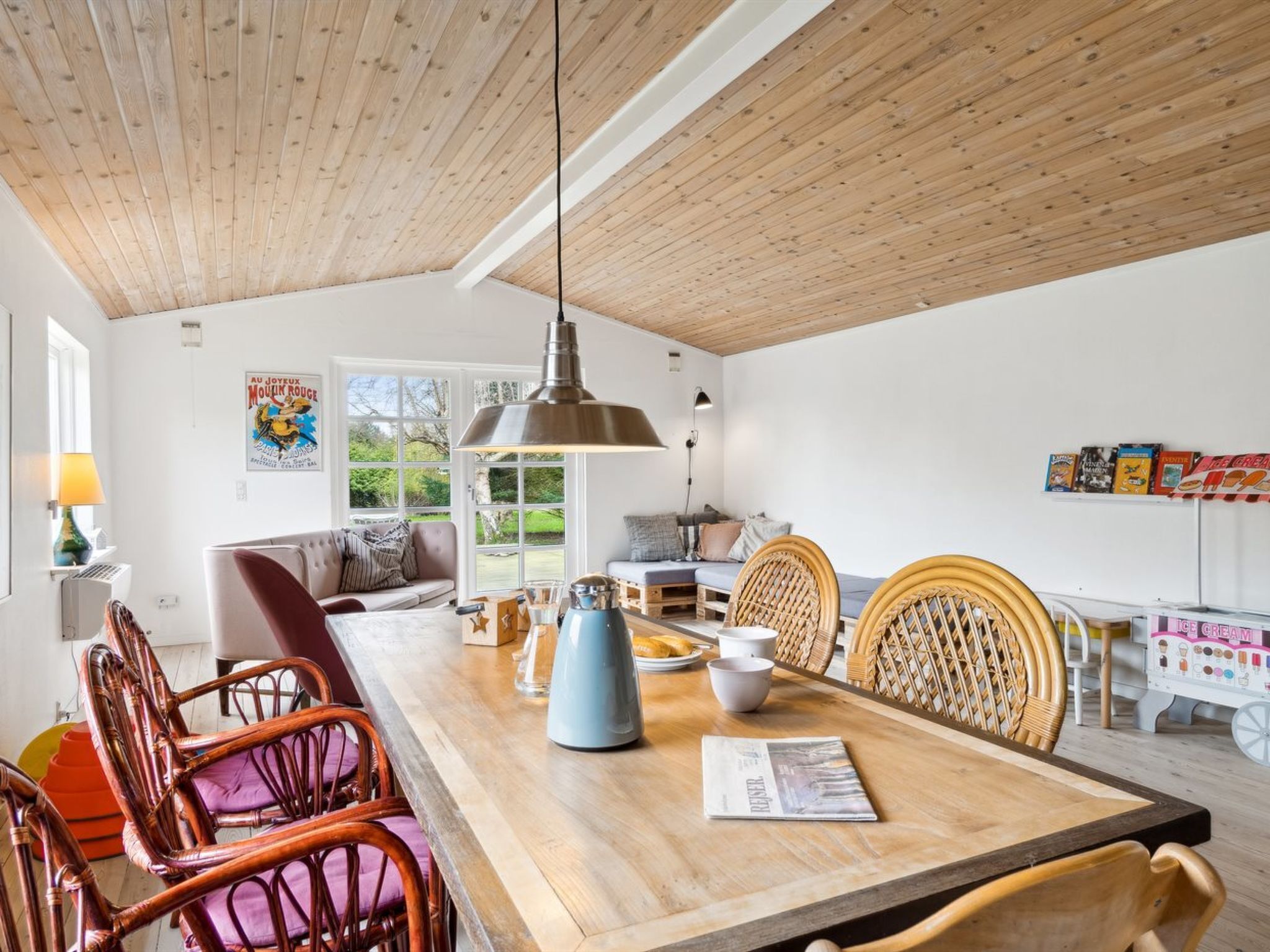 A dining area with a wooden table, wicker chairs, and a hanging light fixture.