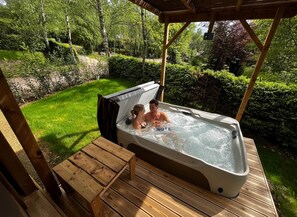 A hot tub on a wooden deck with a view of a garden and trees.