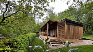 A wooden cabin with a covered porch, surrounded by lush greenery and a well-maintained lawn.