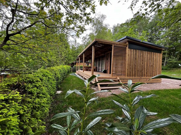 A wooden cabin with a covered porch, surrounded by lush greenery and a well-maintained lawn.