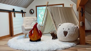 Ein gemütliches Dachzimmer mit Zelt, einem großen Teddybären und einem kleineren Stofftier auf einem flauschigen Teppich.