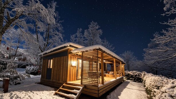 Une charmante cabane en bois dotée d’un porche, entourée d’arbres couverts de neige.