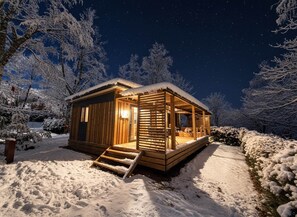 Una cabaña de madera acogedora con un porche, rodeada de árboles cubiertos de nieve.