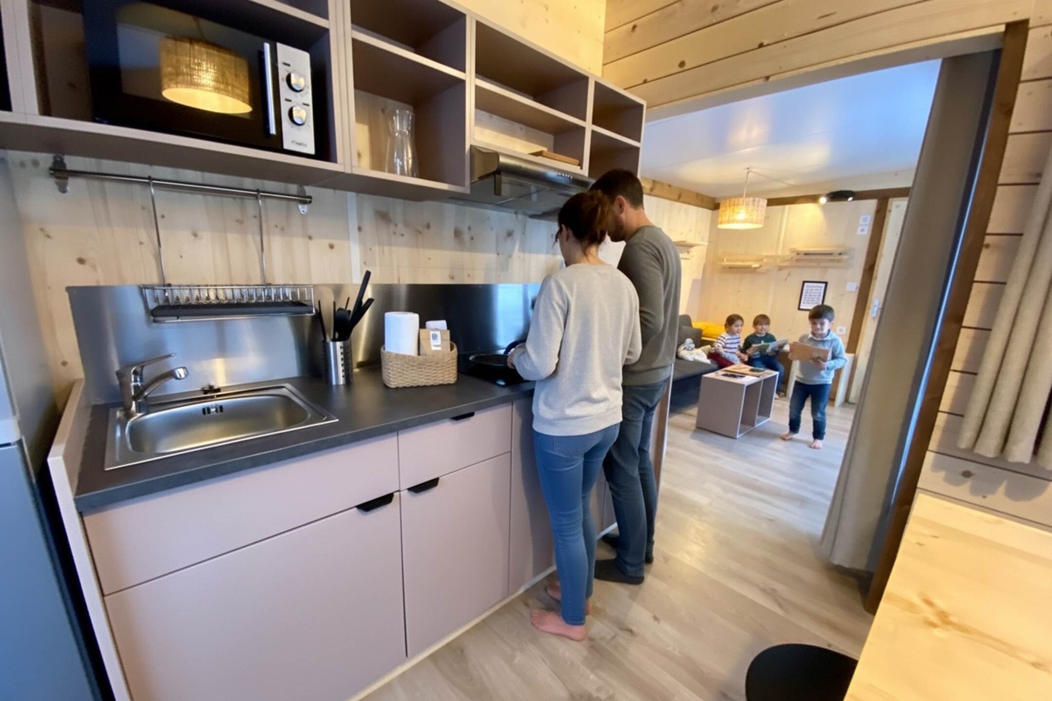 Une cuisine moderne avec un évier en acier inoxydable, des armoires en bois et une cuisinière encastrée. Des étagères au-dessus du plan de travail servent à ranger divers ustensiles de cuisine.