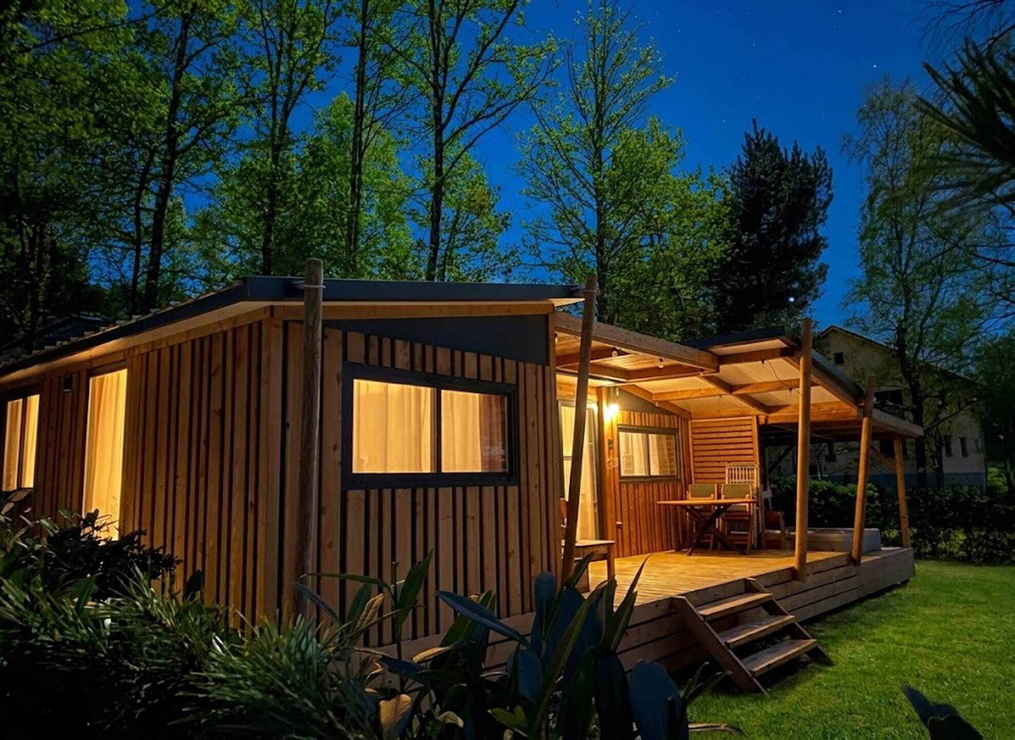 Una cabaña de madera con un porche, ventanas amplias y un espacio al aire libre cubierto.