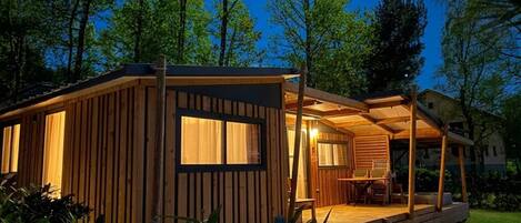 Una cabaña de madera con un porche, ventanas amplias y un espacio al aire libre cubierto.
