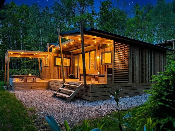 A wooden cabin with a porch, a staircase, and a gravel driveway.