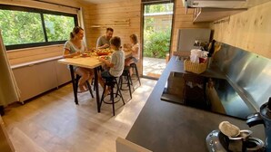 Una famiglia a tavola in una cucina moderna con pareti in legno, un'ampia finestra e un piano cottura in acciaio inossidabile.