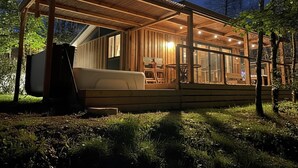 A wooden cabin with a covered porch, a sofa, and a dining table.