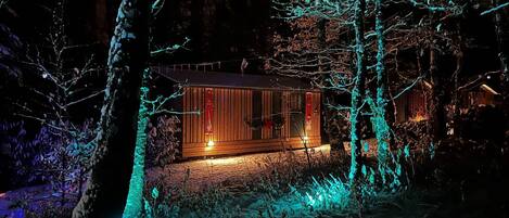 Una cabaña de madera rodeada de árboles, iluminada por luces cálidas.